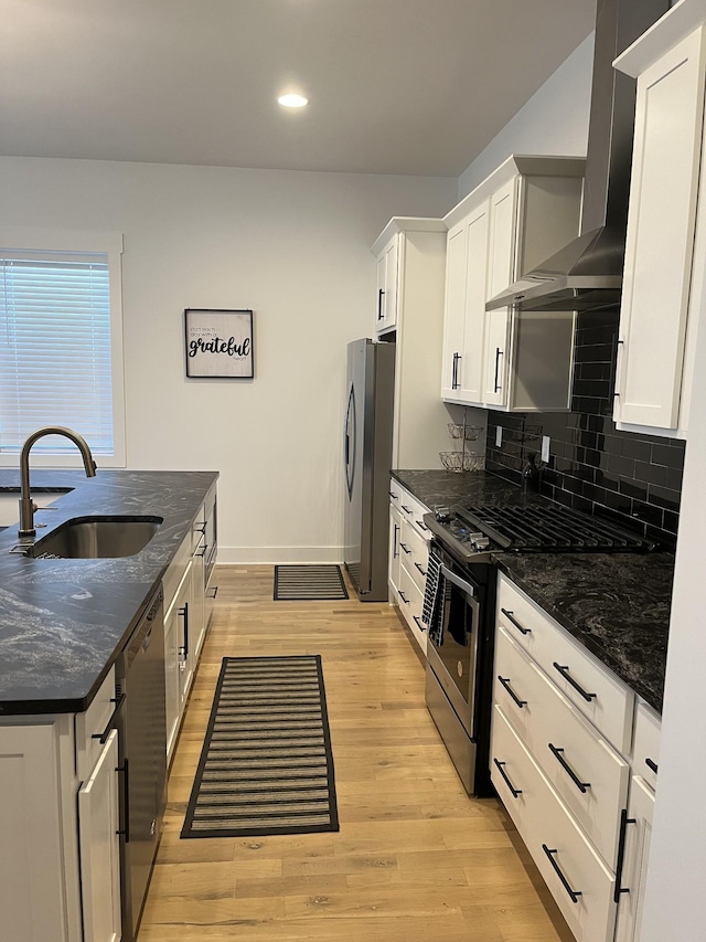 kitchen with light wood finished floors, a sink, appliances with stainless steel finishes, wall chimney range hood, and tasteful backsplash