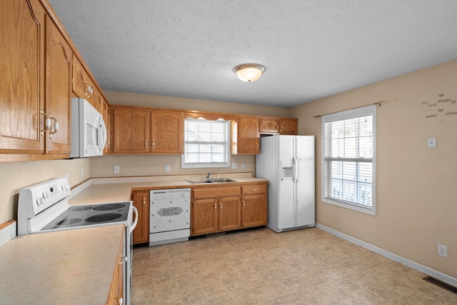 kitchen featuring white appliances, brown cabinetry, visible vents, a sink, and light countertops