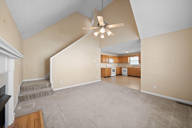 unfurnished living room featuring a ceiling fan, stairway, a fireplace, baseboards, and light colored carpet