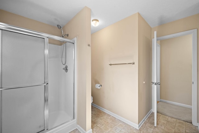 bathroom featuring a stall shower, toilet, and baseboards