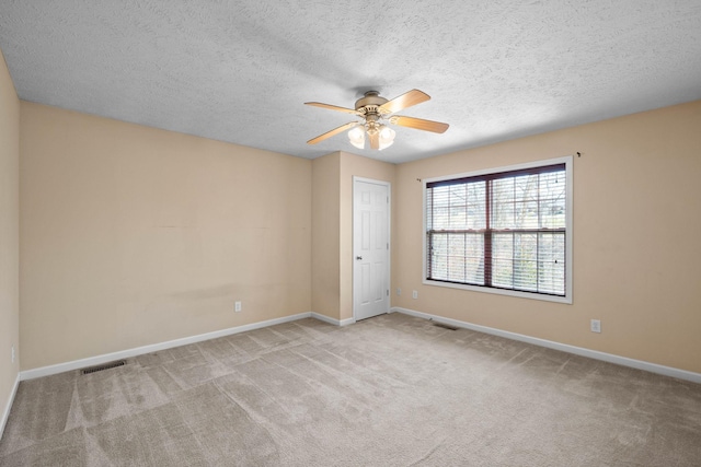 spare room featuring carpet, a ceiling fan, visible vents, baseboards, and a textured ceiling