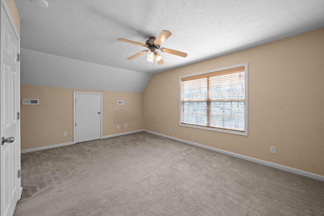 additional living space featuring visible vents, lofted ceiling, light carpet, a textured ceiling, and a ceiling fan