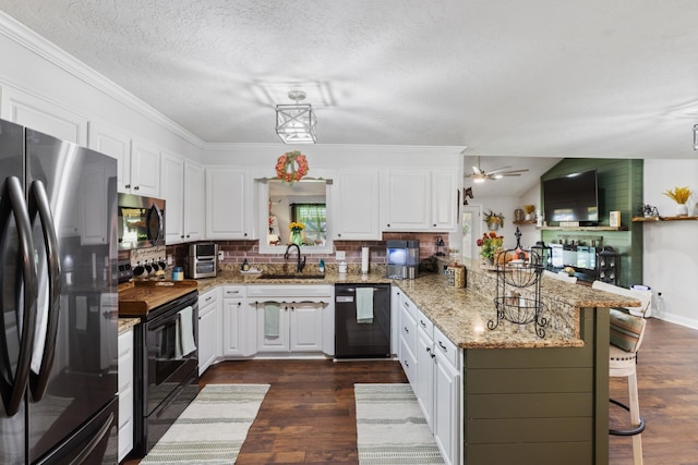 kitchen featuring a peninsula, a sink, black appliances, dark wood-type flooring, and a kitchen breakfast bar