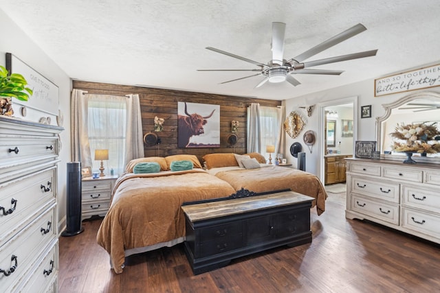 bedroom with a ceiling fan, a textured ceiling, wood finished floors, connected bathroom, and wooden walls