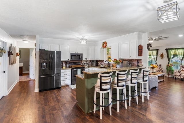 kitchen featuring light stone counters, a peninsula, black appliances, white cabinets, and dark wood-type flooring