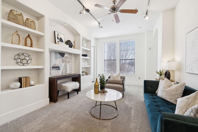 living room with track lighting, a ceiling fan, built in features, carpet floors, and baseboards