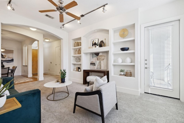 sitting room with visible vents, built in shelves, ceiling fan, carpet flooring, and arched walkways