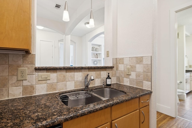 kitchen with dark stone countertops, tasteful backsplash, visible vents, and a sink