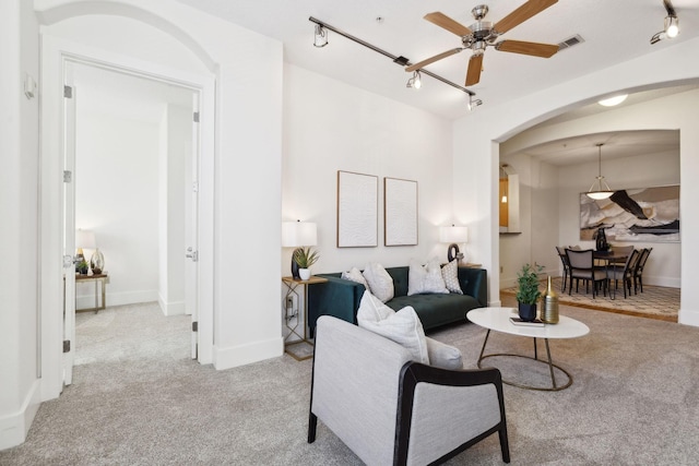 living room featuring baseboards, carpet floors, arched walkways, ceiling fan, and rail lighting