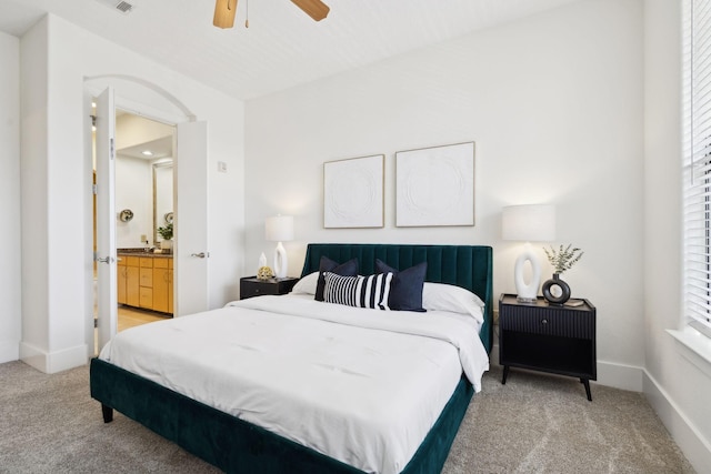 bedroom with light carpet, ensuite bath, baseboards, and a ceiling fan