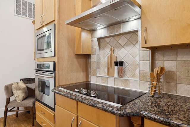 kitchen featuring visible vents, dark stone countertops, backsplash, appliances with stainless steel finishes, and wall chimney range hood