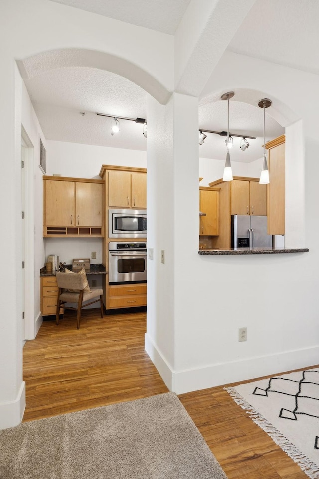 kitchen with light wood-style flooring, arched walkways, light brown cabinetry, appliances with stainless steel finishes, and a textured ceiling