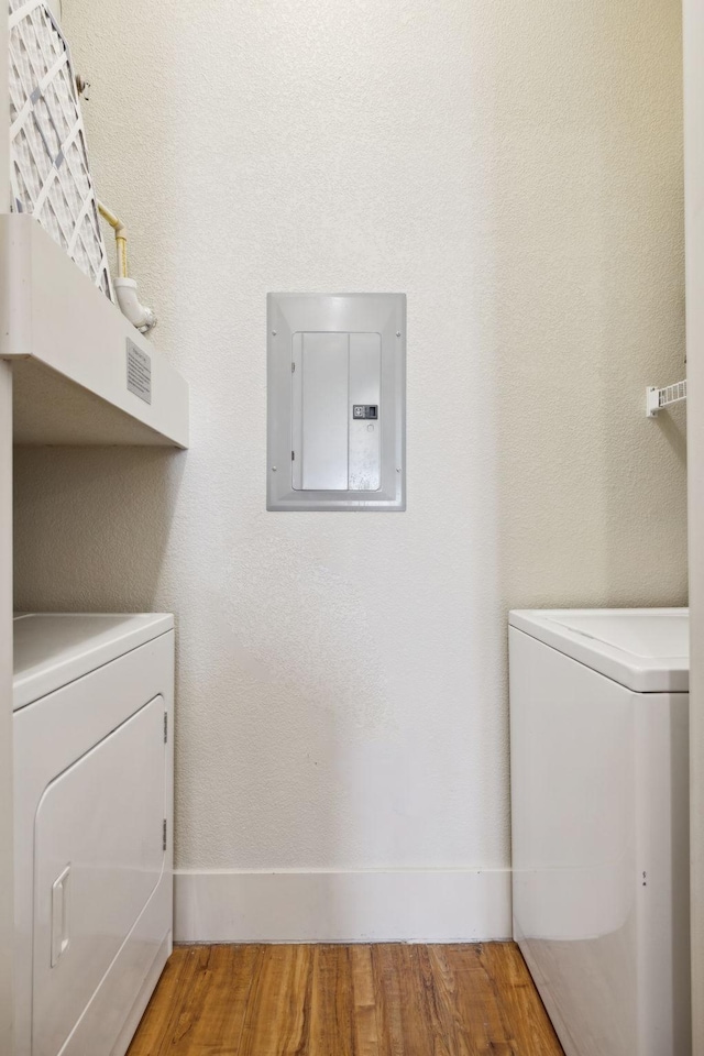 clothes washing area with baseboards, washing machine and dryer, electric panel, laundry area, and wood finished floors