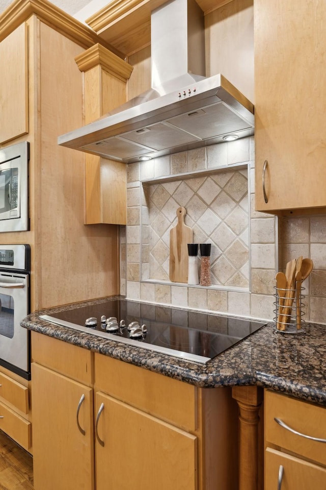 kitchen featuring wood finished floors, dark stone counters, decorative backsplash, appliances with stainless steel finishes, and wall chimney range hood