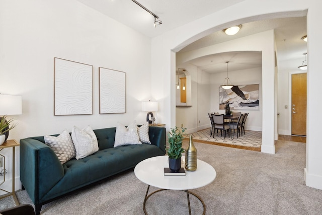 carpeted living room featuring baseboards, arched walkways, and track lighting