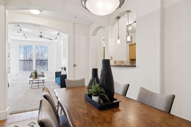 dining room featuring arched walkways, track lighting, light colored carpet, and ceiling fan