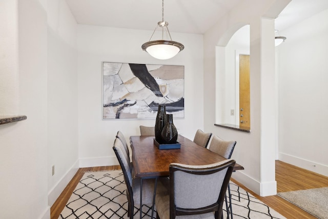 dining area featuring wood finished floors, arched walkways, and baseboards