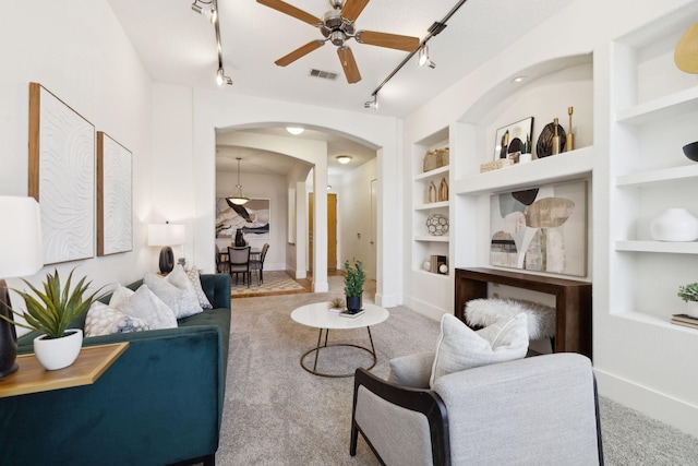 living area featuring built in shelves, carpet, visible vents, arched walkways, and ceiling fan