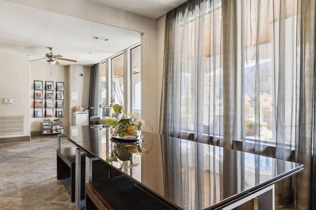 dining area with visible vents, a textured ceiling, stone finish flooring, and ceiling fan