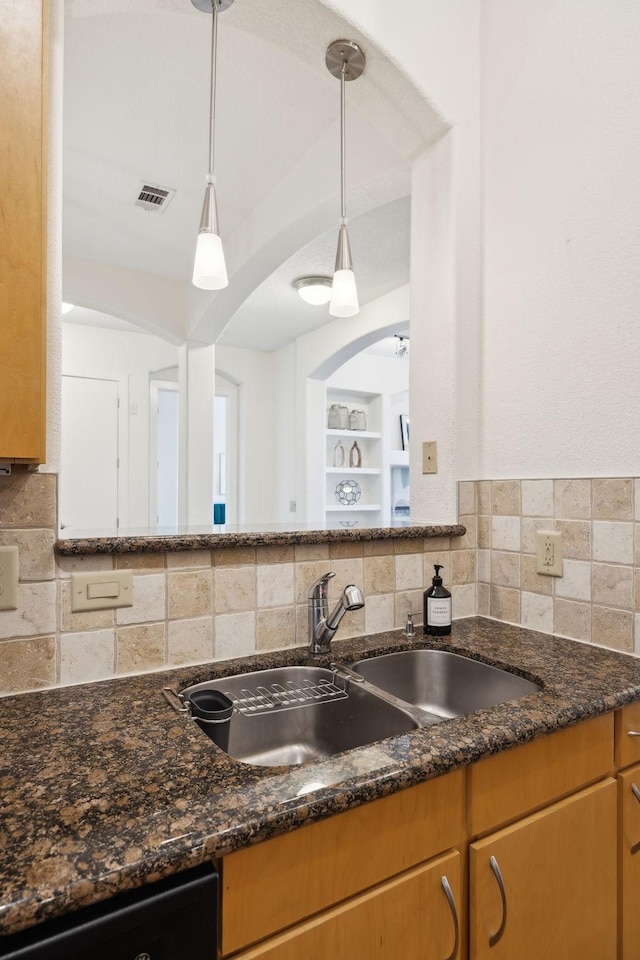 kitchen featuring dishwasher, dark stone countertops, tasteful backsplash, and a sink