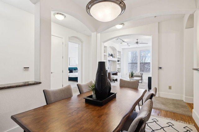 dining room with light wood-type flooring, built in features, arched walkways, baseboards, and ceiling fan