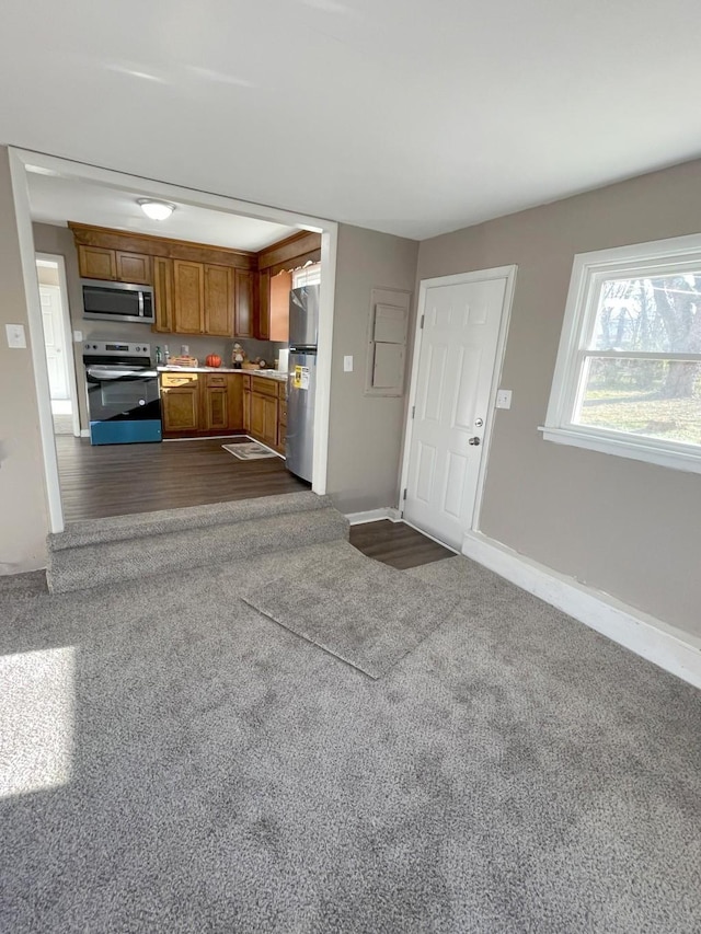 kitchen with brown cabinets, dark carpet, stainless steel appliances, light countertops, and baseboards