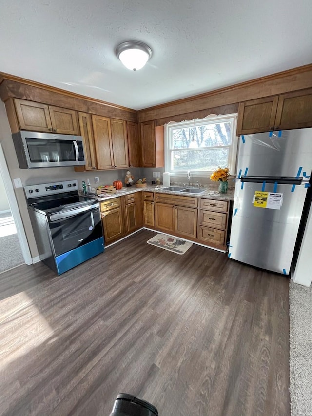 kitchen with brown cabinetry, a sink, stainless steel appliances, light countertops, and dark wood-type flooring