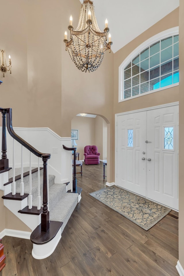 entrance foyer with stairs, a high ceiling, wood finished floors, arched walkways, and a notable chandelier