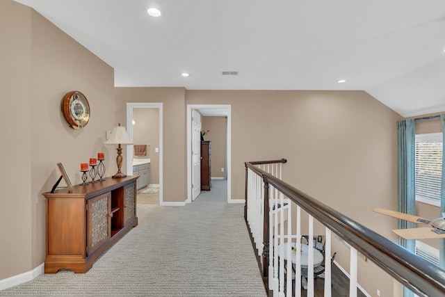 hall with an upstairs landing, visible vents, light carpet, and baseboards