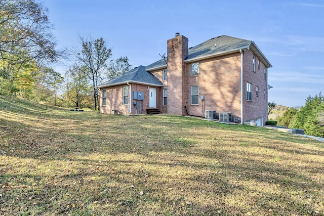 back of house with brick siding, central air condition unit, a lawn, and a chimney