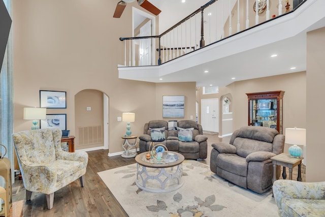 living room with a ceiling fan, wood finished floors, visible vents, arched walkways, and a towering ceiling