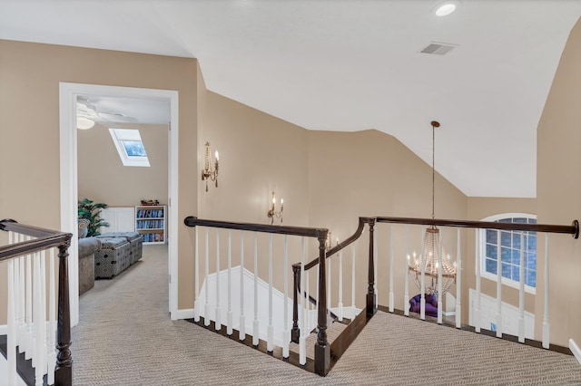 staircase with visible vents, vaulted ceiling with skylight, carpet, an inviting chandelier, and baseboards