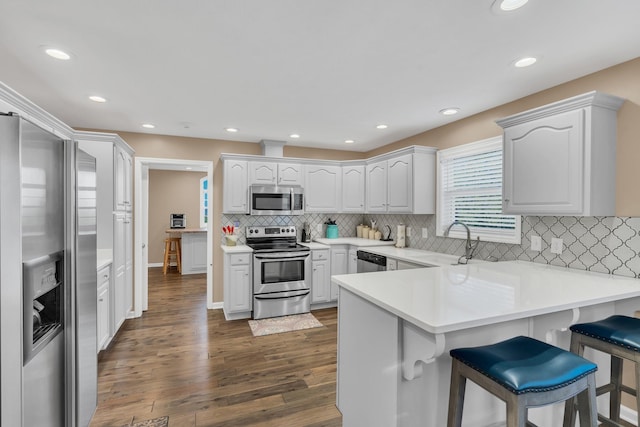 kitchen featuring a sink, a kitchen breakfast bar, dark wood finished floors, appliances with stainless steel finishes, and a peninsula