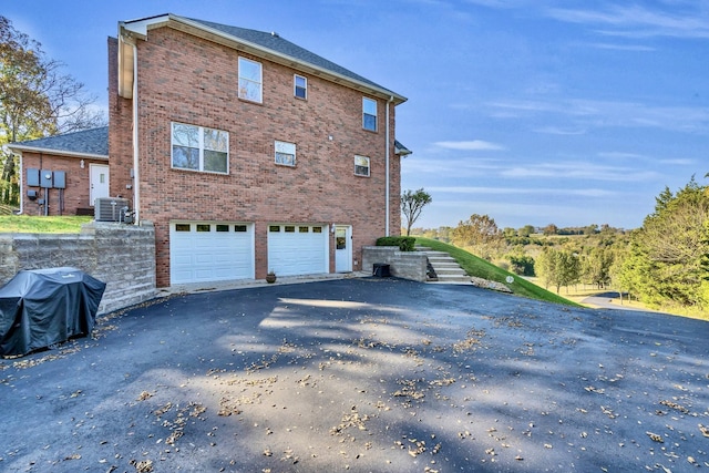 view of property exterior featuring a garage, brick siding, central AC, and driveway