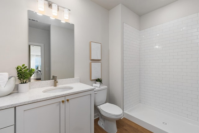 bathroom with visible vents, toilet, wood finished floors, a tile shower, and vanity