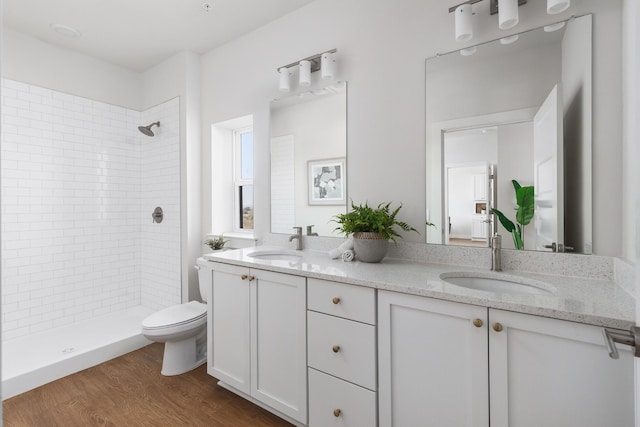 bathroom with toilet, wood finished floors, a tile shower, and a sink