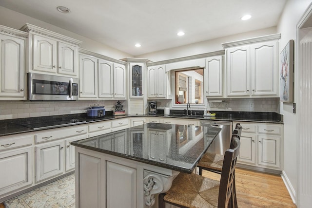 kitchen with dark stone counters, a kitchen bar, light wood-style floors, stainless steel appliances, and a sink