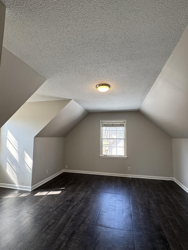 additional living space featuring dark wood-style floors, a textured ceiling, baseboards, and vaulted ceiling