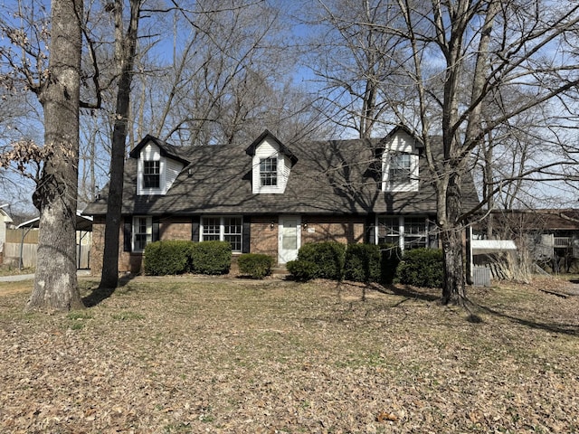 cape cod-style house featuring brick siding, a shingled roof, and fence