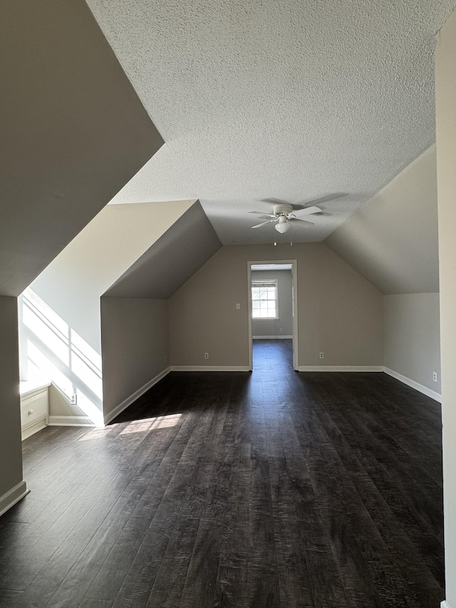 bonus room featuring a ceiling fan, a textured ceiling, dark wood-style floors, baseboards, and vaulted ceiling