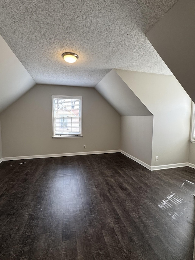 additional living space with dark wood-style floors, a textured ceiling, baseboards, and vaulted ceiling