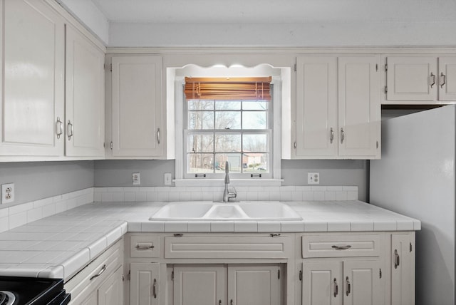 kitchen with white cabinets, freestanding refrigerator, and a sink