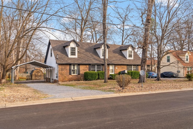 new england style home featuring gravel driveway, brick siding, a detached carport, and roof with shingles