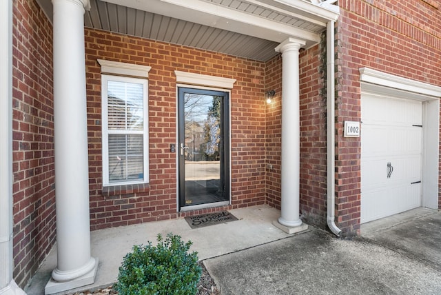 view of exterior entry featuring a garage and brick siding