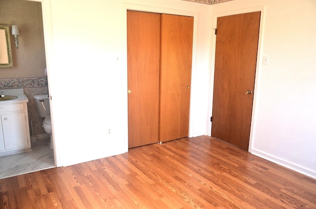 unfurnished bedroom with a sink, a closet, light wood-style floors, and ensuite bathroom