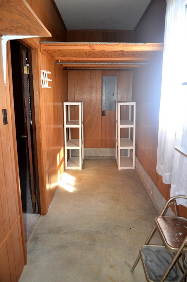 hallway featuring wooden walls, electric panel, and unfinished concrete flooring