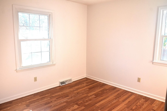 unfurnished room featuring dark wood-style floors, visible vents, a healthy amount of sunlight, and baseboards