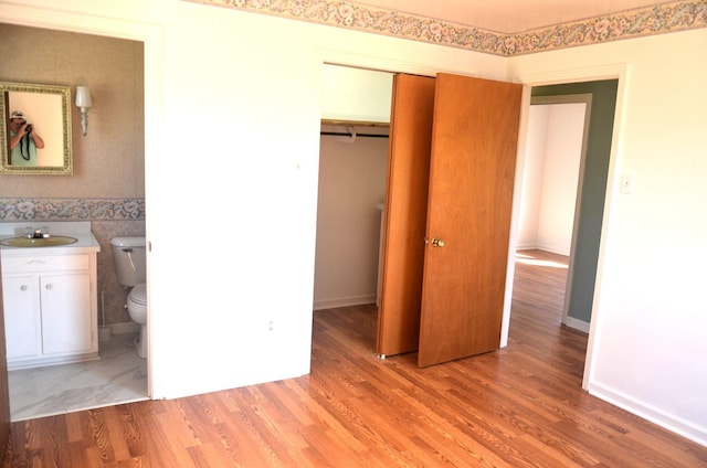 unfurnished bedroom with a sink, ensuite bath, a closet, wainscoting, and light wood finished floors