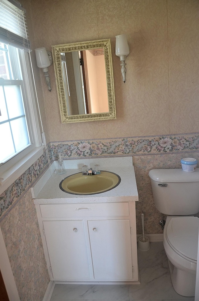 bathroom featuring toilet, marble finish floor, vanity, and wallpapered walls