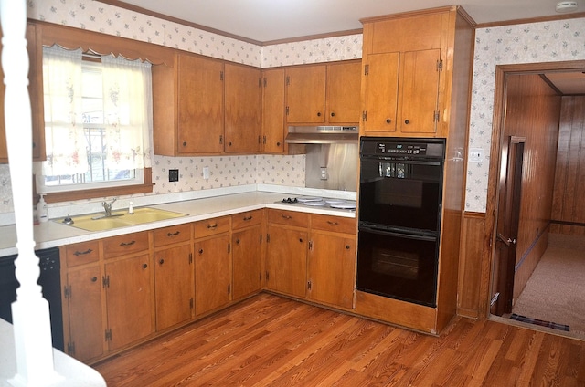 kitchen with wallpapered walls, a sink, light wood-style floors, under cabinet range hood, and dobule oven black